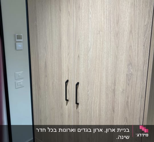 ארון בגדים מעץ בהיר עם דלתות ציר, ידיות שחורות ומראה ממוסגרת
